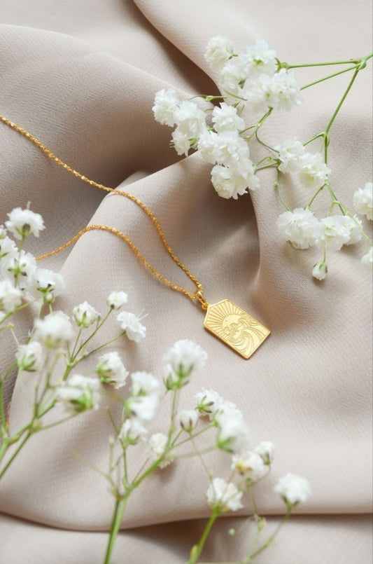 Gold necklace with a pendant on a beige fabric background with white flowers.